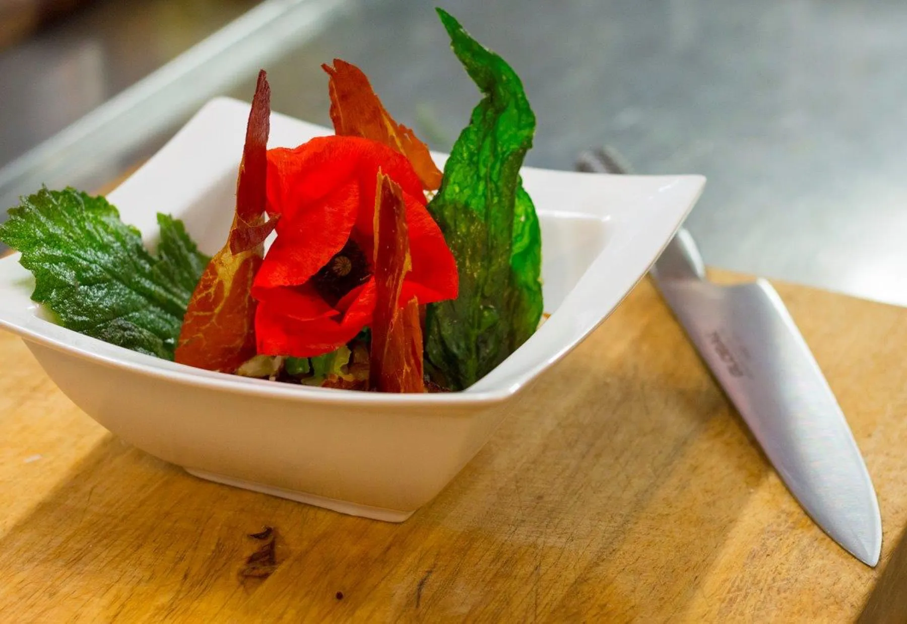 A colourful starter in a white bowl, next to a chef’s knife